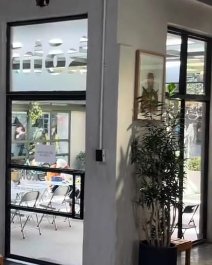 The glass entrance at Kōhī with the wordmark etched on the door, a framed print on the plaster pillar beside a potted plant, opening onto the 44 Stanley courtyard.